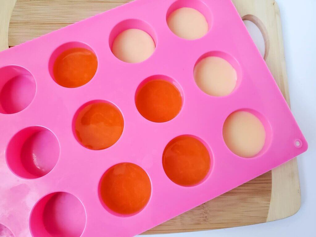 Image of a pink silicone mold with solid lotion bars as well as fresh ones.