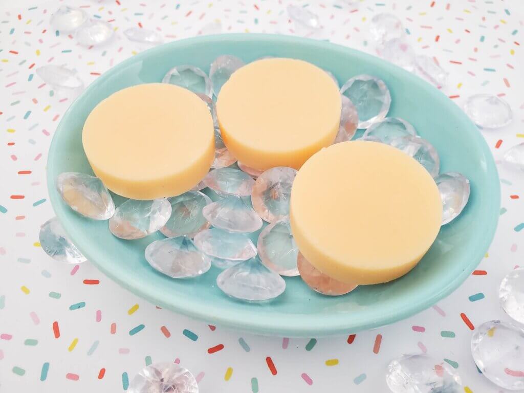 Now you know how to make mango lotion bars that smell like Hawaii! Image of 3 yellow mango lotion bars in a blue dish.