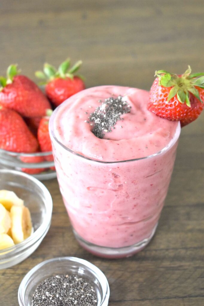 Learn how to make this mango straweberry banana smoothie with chia seeds by top Hawaii blog Hawaii Travel with Kids. Image of a pink smoothie in a glass surrounded by bowls of strawberries, banana, and chia seeds.