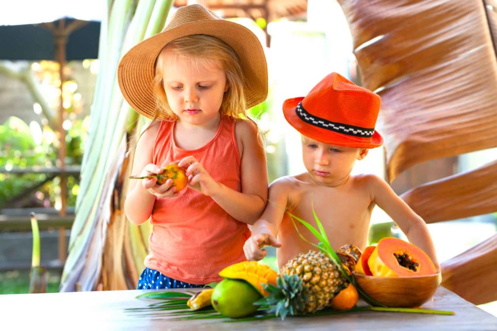 Find out the best Oahu babysitting services recommended by top Hawaii blog Hawaii Travel with Kids. Image of 2 kids tasting tropical fruit in Hawaii.