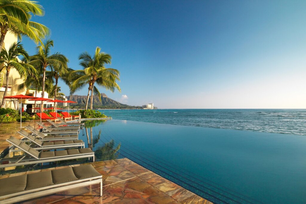 The Sheraton Waikiki is one of the Best Resorts in Oahu for Families wanting to stay in Waikiki. Image of some lounge chairs at the infinity pool at Waikiki Beach.