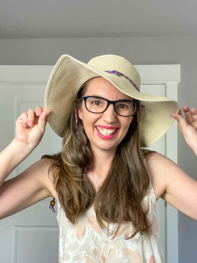 Image of a woman wearing glasses while trying on a straw sun hat from a Wantable subscription box.