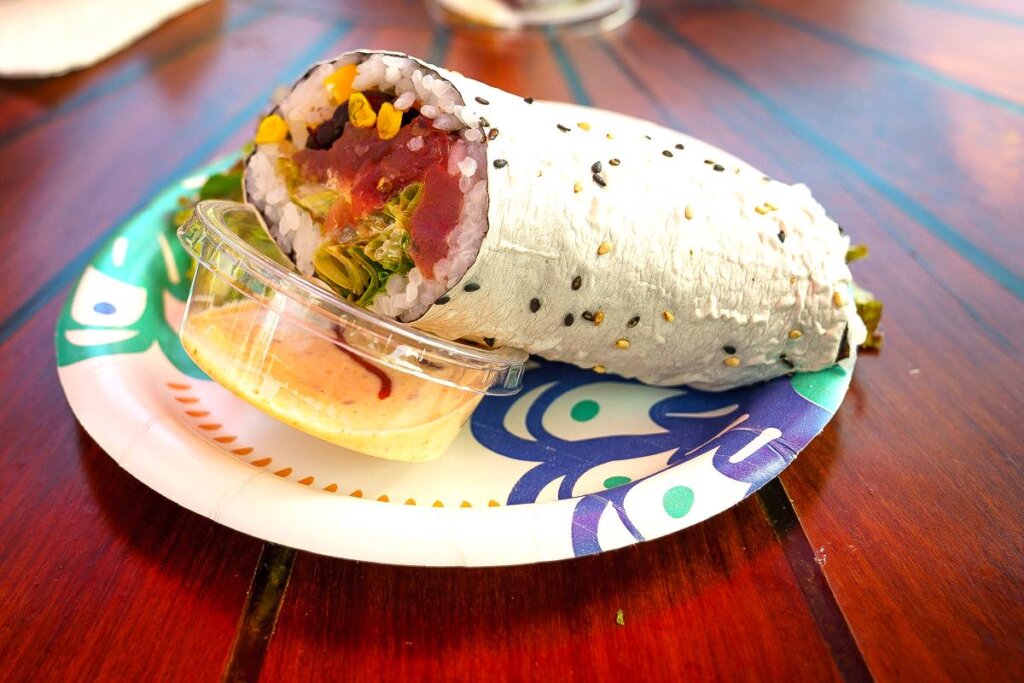 Doing a Kauai Food Tour is a top things to do on Kauai with kids. Image of a sushi burrito on a paper plate.