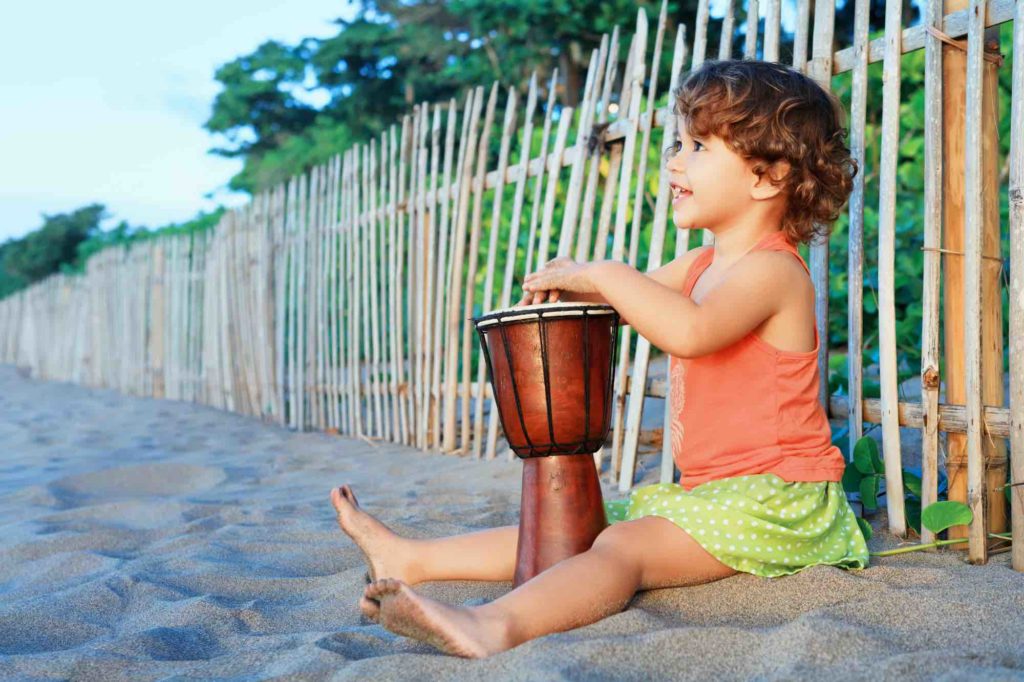 Find out the best babysitters in Maui recommended by top Hawaii blog Hawaii Travel with Kids. Image of a little girl playing a drum on a beach.