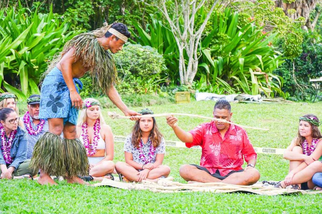 This Samoan kava ceremony is one of the reasons why Toa Luau is one of the best luaus in Oahu Hawaii. Image of a man handing a stick to a Samoan chief who is sitting on the grass.