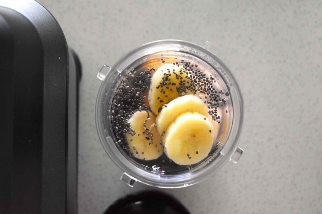 Place all the blueberry banana chia smoothie ingredients in the blender. Image of a blender with banana, chia seeds, blueberries, and honey inside.