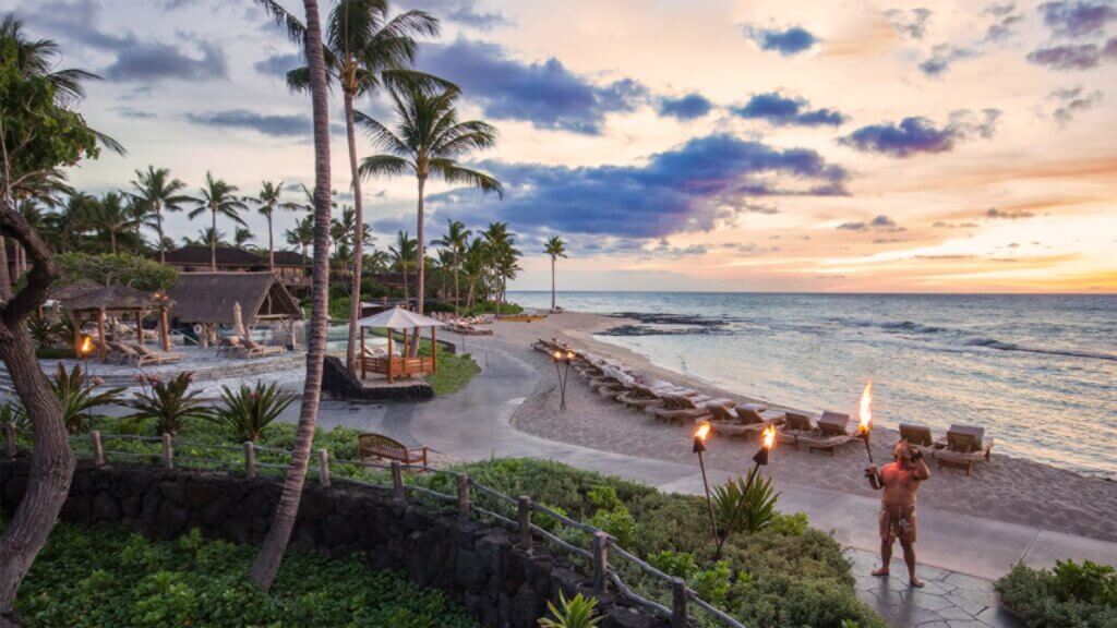 The Four Seasons Resort Hualalai tops our list of where to stay in Big Island with kids. Image of a torch lighting ceremony on the beach in Hawaii.