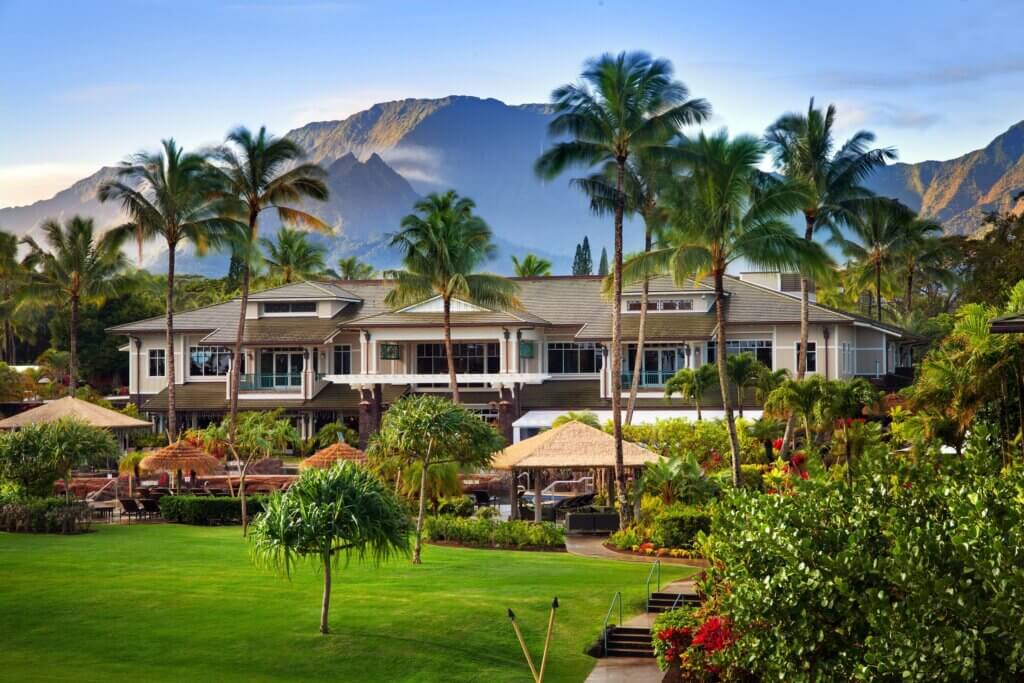 The Westin Princeville Ocean Resort Villas is one of the best resorts in Kauai for families because of its stunning location. Image of a resort in front of the mountains on Kauai.