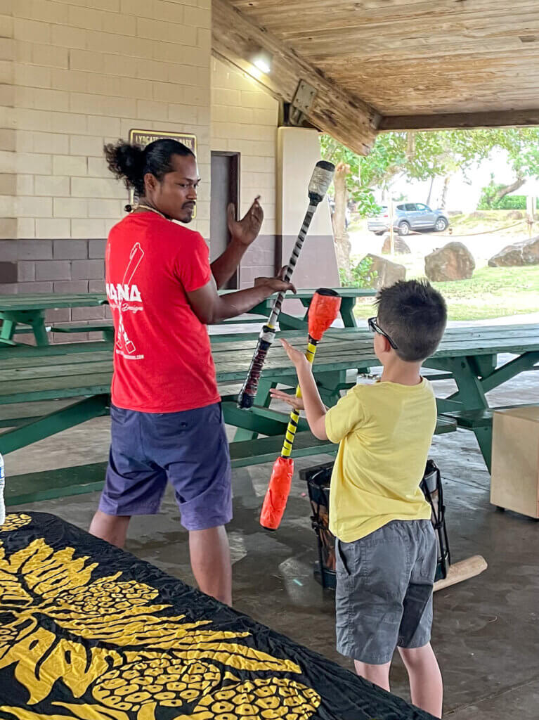 Image of a man teaching a boy how to do Hawaiian fire knife dancing.