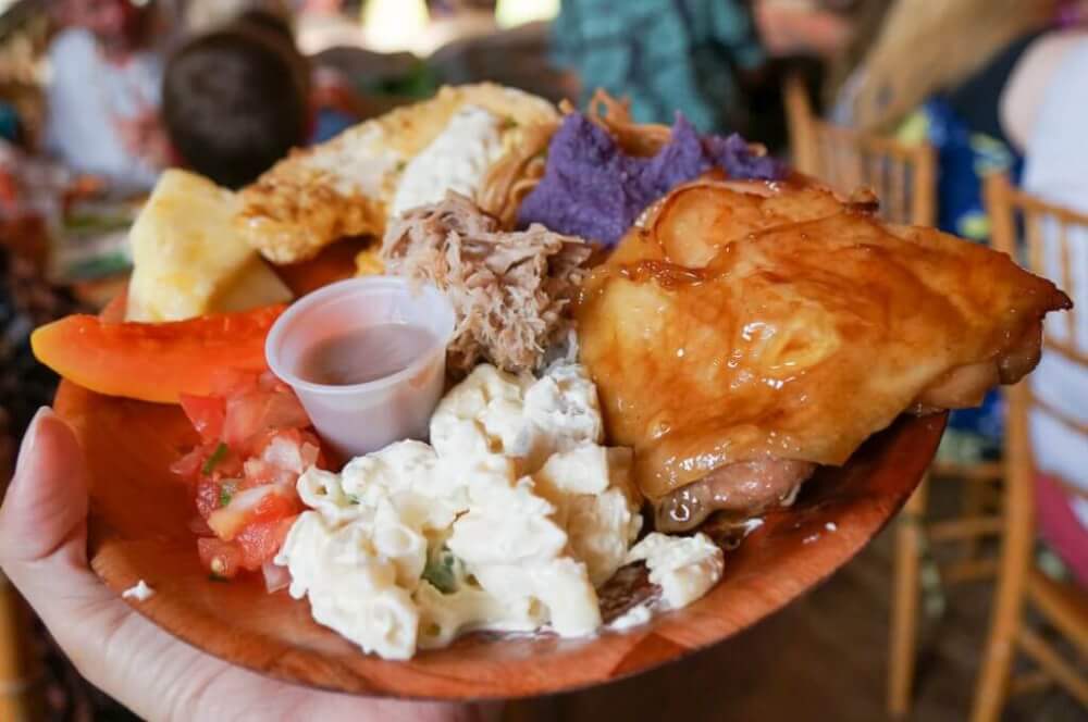 Luau Kalamaku has some of the best luau food on Kauai! Image of a plate with chicken, kalua pork, lomi lomi salmon, macaroni salad, and more!