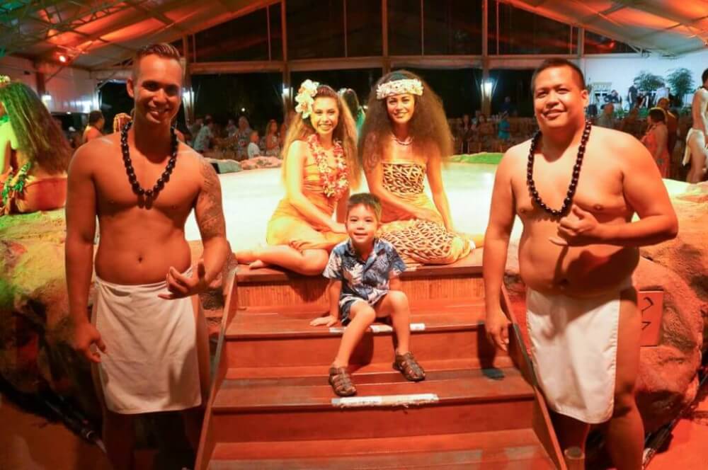 Luau Kalamaku is a kid friendly Kauai luau. Image of a boy posing with a bunch of hula dancers.