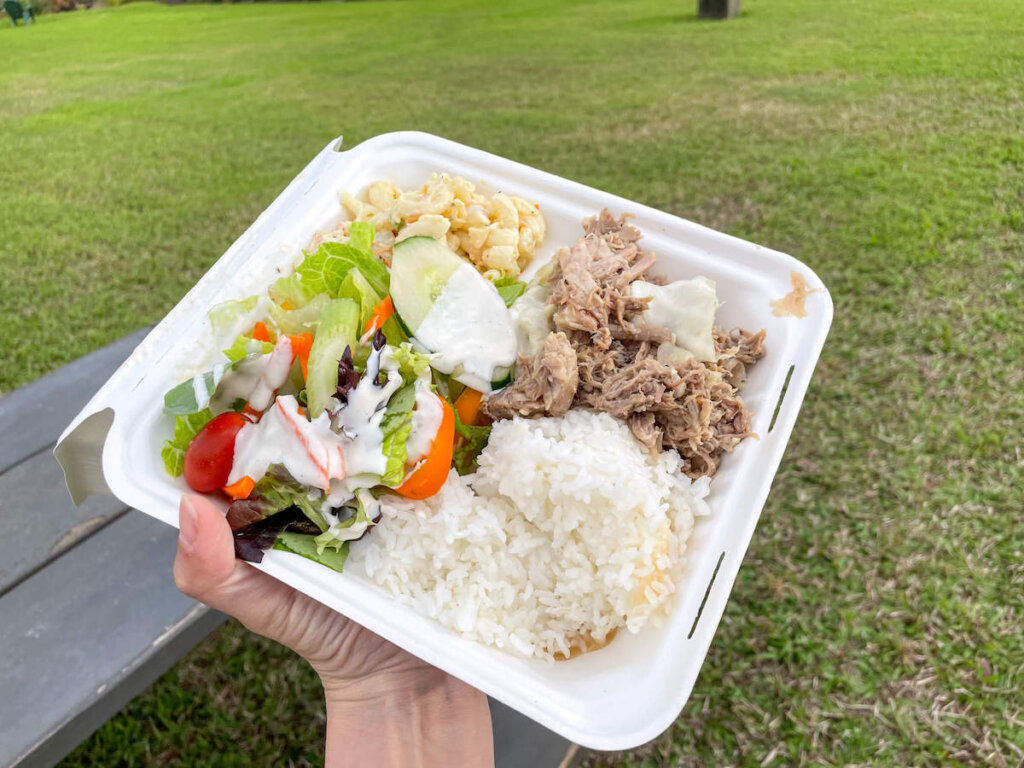 You'll get tasty Kauai luau food at this Hawaiian fire dancer show in North Shore Kauai. Image of a takeout container with kalua pork, macaroni salad, green salad, and rice.