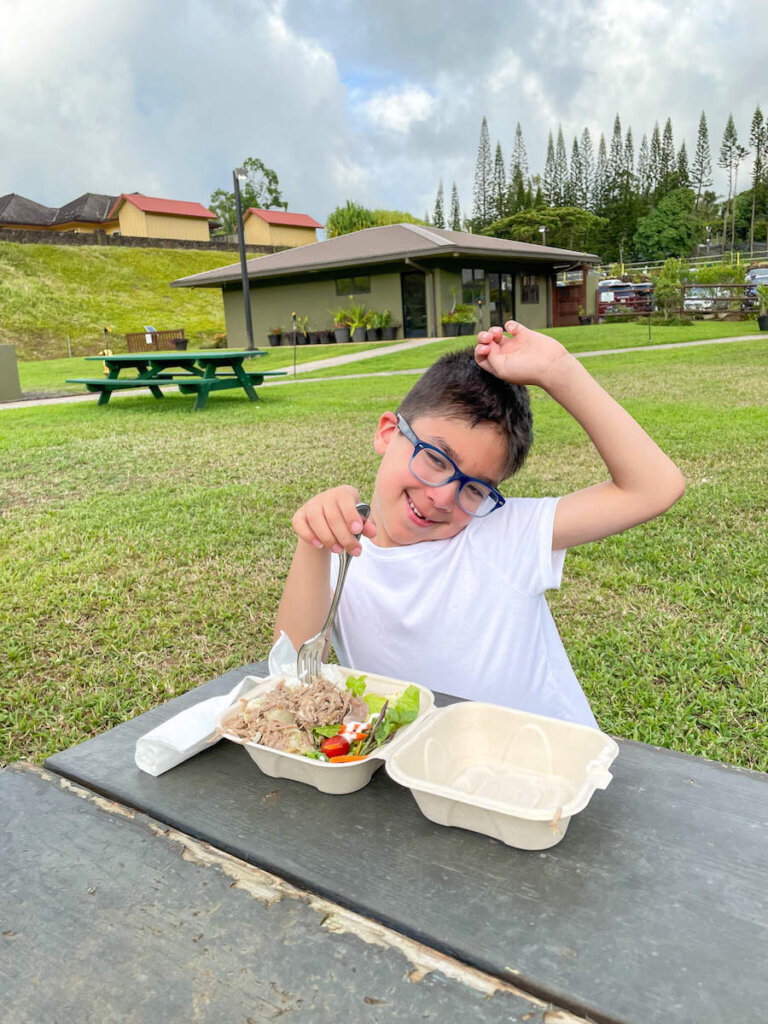 The food at the Ahi Lele Kauai luau is super tasty. Image of a boy posing with his Hawaiian plate lunch at Anaina Hou Community Park.