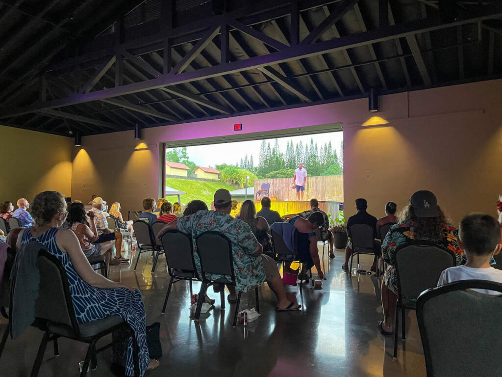 In June 2021, the Ahi Lele Fire Show seating included spaced out chairs inside the pavilion. Image of people sitting in chairs that are socially distanced.