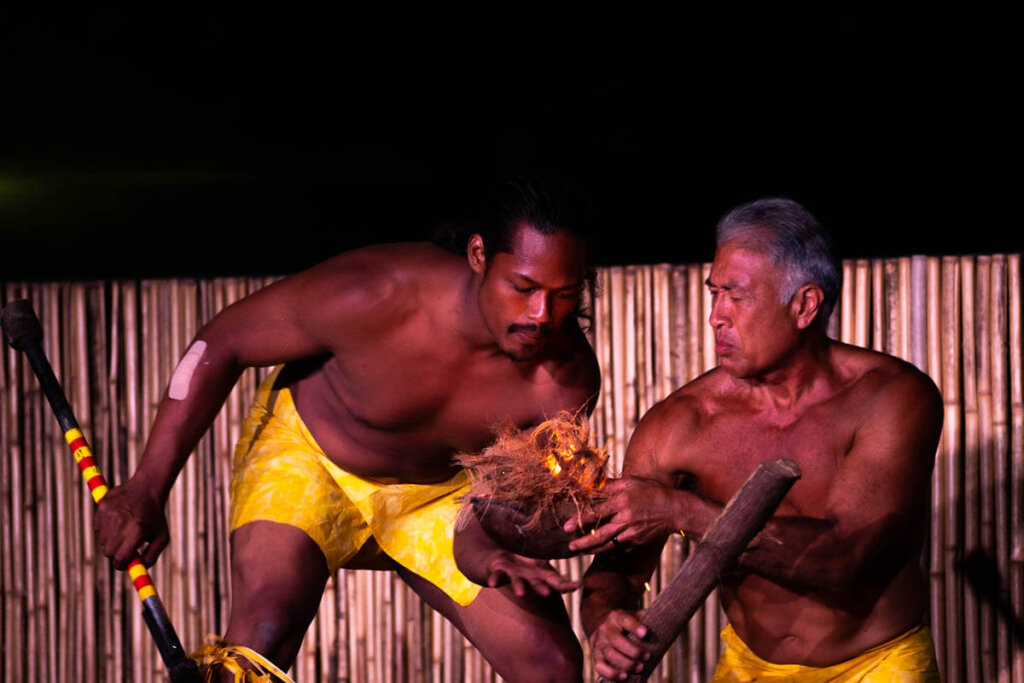 Learn how to make a fire using coconut husks on Kauai. Image of two men marveling at coconut husks on fire.