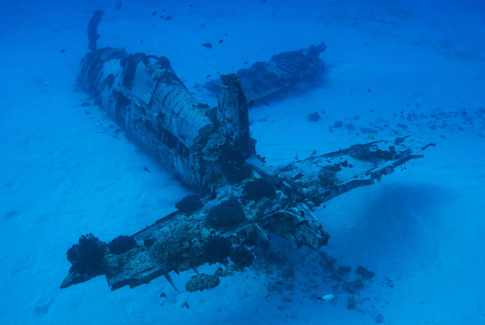 Want to explore Hawaii off the beaten path? Check out the Corsair Plane Wreck dive site, one of the best hidden gems in Hawaii. Image of a sunken plane.