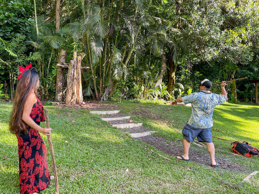 Learn how to throw a Hawaiian spear at the Experience Nutridge Luau on Oahu. Image of a man wearing an Aloha shirt throwing a spear at a target.