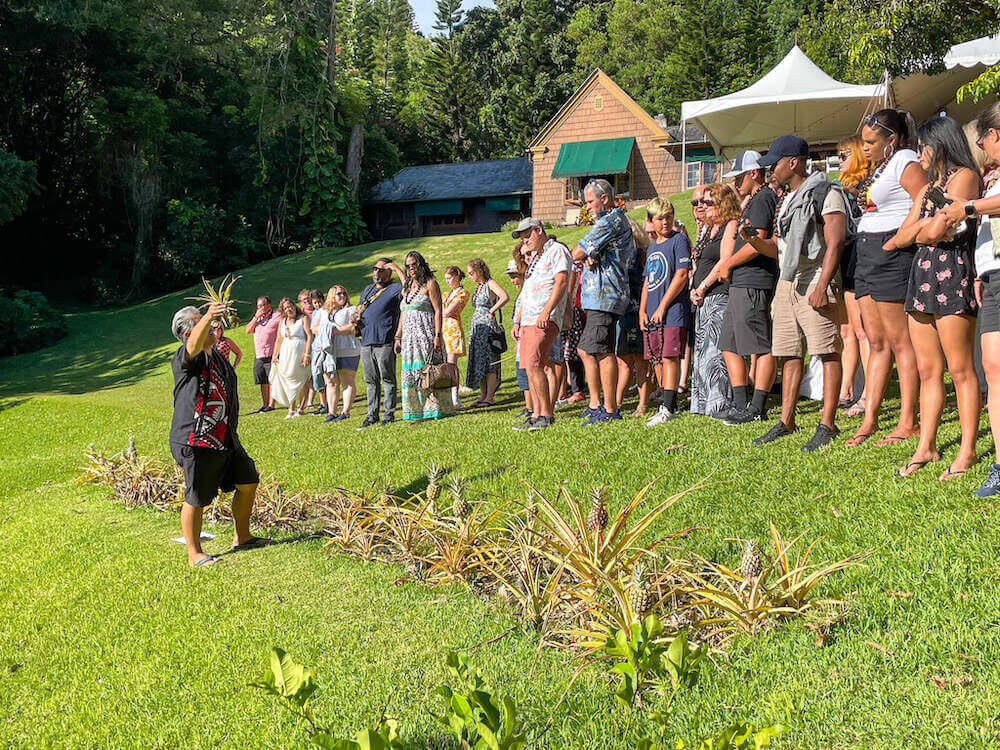 Learn the history of the pineapple at Nutridge Estate on Oahu. Image of a man holding a pineapple in front of a crowd of tourists.