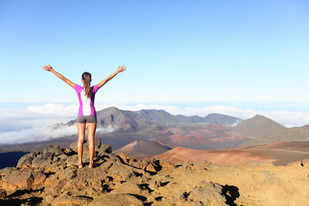 Find out the best Haleakala tours on Maui recommended by top Hawaii blog Hawaii Travel with Kids. Image of a woman standing on the summit of Haleakala Crater at Haleakala National Park.