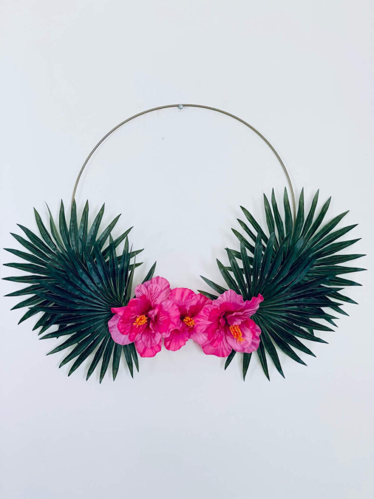 Image of a gold hoop wreath with palm leaves and pink hibiscus flowers on it.
