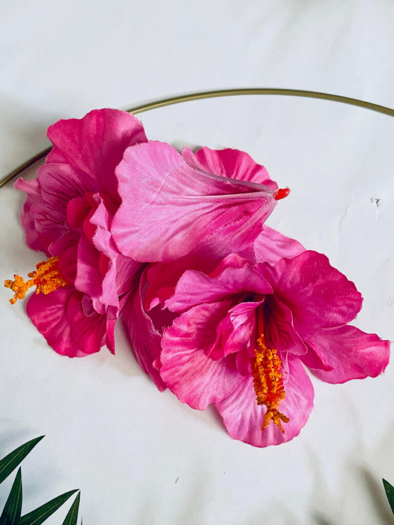 Image of three pink silk hibiscus blossoms on a white surface.