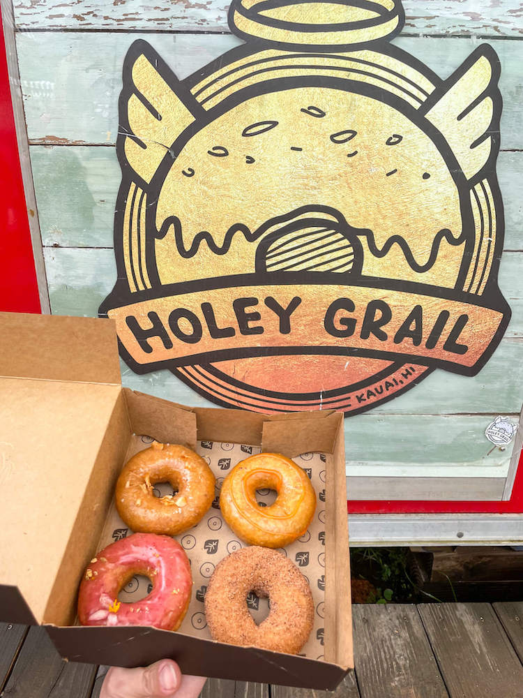 One of the best places to eat in Hanalei for breakfast is Holey Grail food truck. Image of a box of 4 donuts in front of the Holey Grail food truck sign.