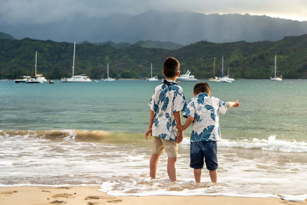 Your Kauai photographer will have lots of posing tips. Image of two boys holding hands facing the ocean on Kauai.