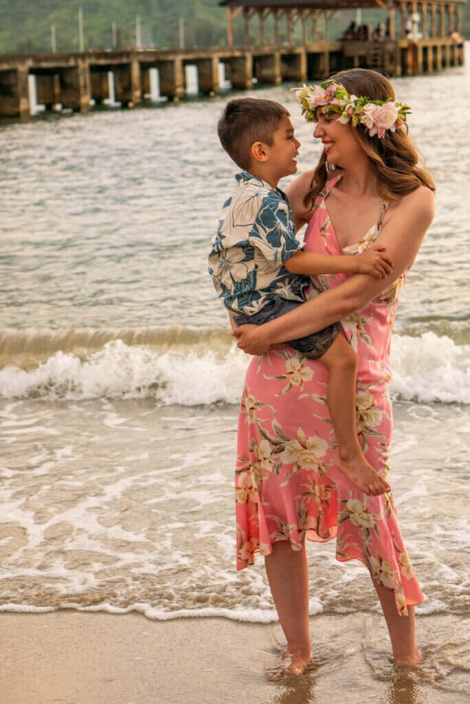 Image of a woman wearing a pink Hawaiian dress holding a boy wearing a blue Aloha shirt at Hanalei Pier on Kauai.