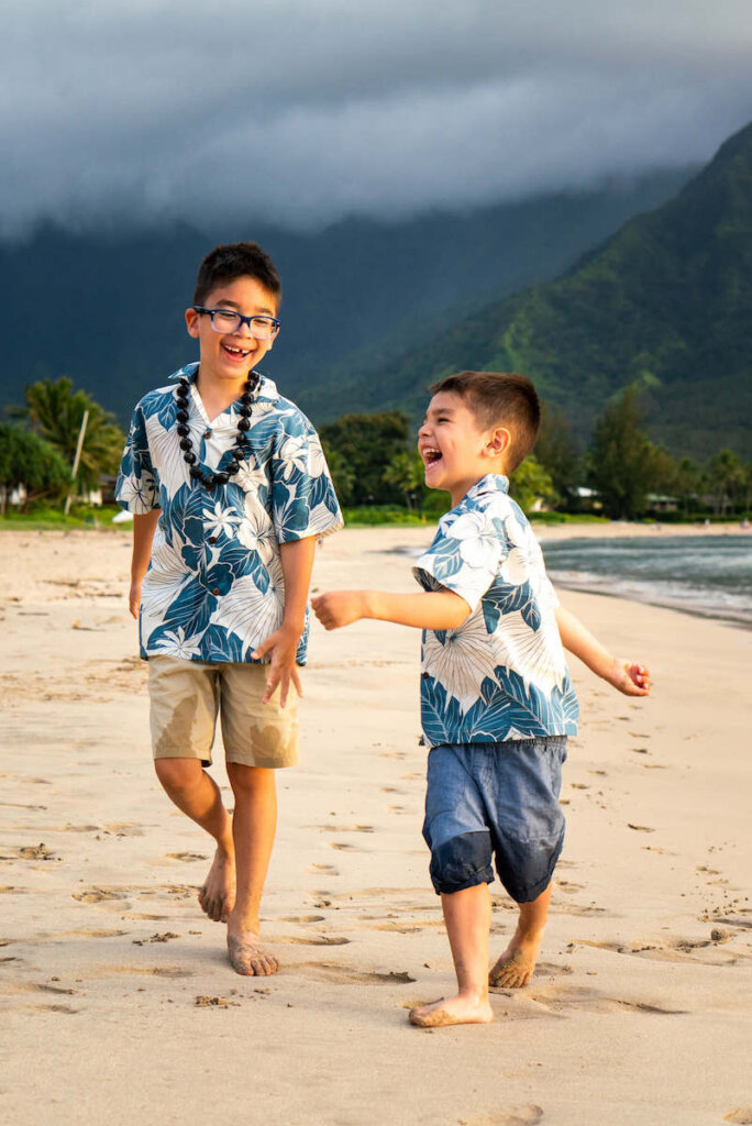 Get the cutest Hawaii family photography by booking a Flytographer photo shoot on Kauai. Image of two boys wearing Hawaiian shirts running on the beach laughing.