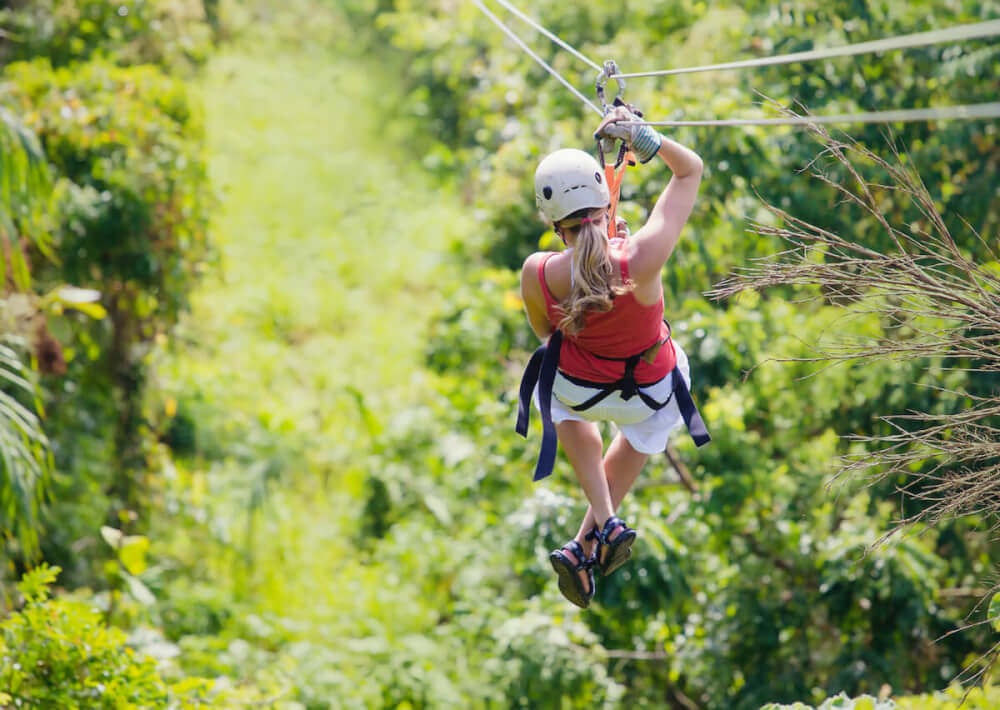 Find out the best Kauai ziplines recommend by top Hawaii blog Hawaii Travel with Kids. Image of the backside of a woman ziplining in Hawaii.