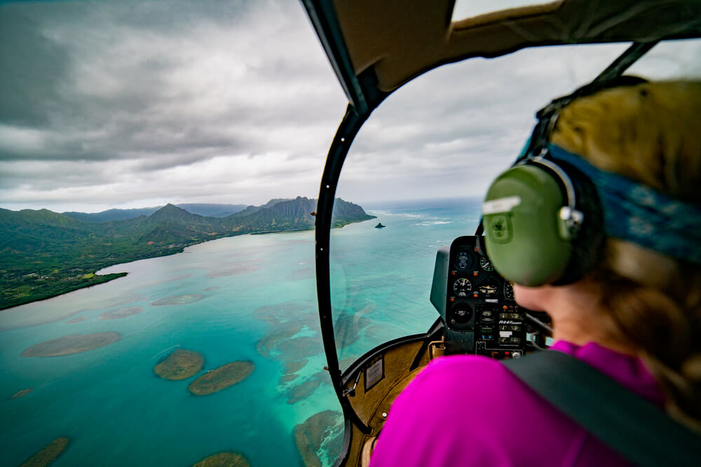 One of the most popular tours in Honolulu is going on an Oahu helicopter ride. Image of a woman wearing head phones inside a helicopter.