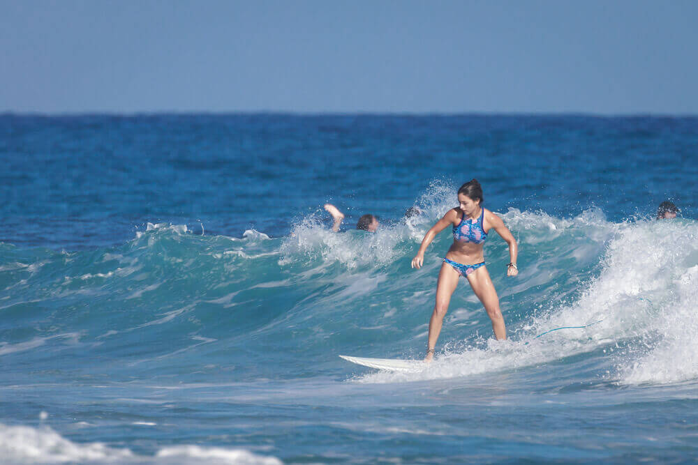 Find out where to go surfing in Maui Hawaii by top Hawaii blog Hawaii Travel with Kids. Image of a girl surfing in the ocean.