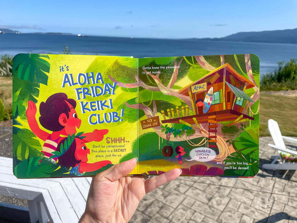 Looking for cute Hawaiian books for kids? Check out The Aloha Friday Keiki Club book by Keiki Kaukau. Image of someone holding open a Hawaiian kids book.