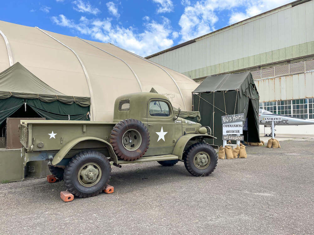 The Pearl Harbor Aviation Museum hosts Bob Hope: An American Treasure traveling exhibit. Image of a green army truck and a sign that says Bob Hope Commanding Officer of Laughter.