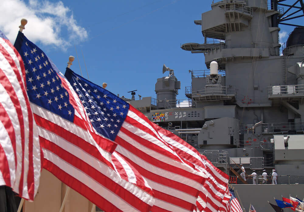 Image of American flags flying in front of the USS Battleship Missouri at Pearl Harbor on Oahu.