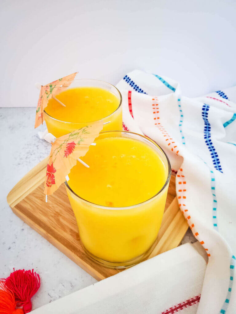 Find out how to make this frozen mango margarita recipe by top Hawaii blog Hawaii Travel with Kids. Image of a bright orange tropical cocktail in 2 glasses with little umbrellas.