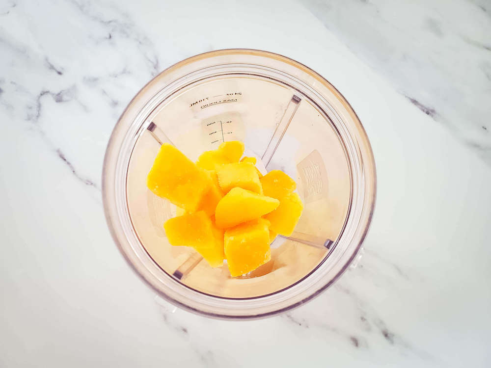 This is an easy frozen mango margarita recipe that only requires 4 ingredients Image of a blender with ice and frozen mango chunks inside.