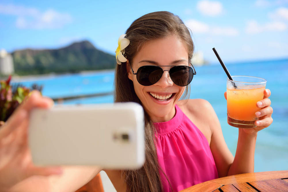 These tropical drink Instagram captions are perfect for your trip to Hawaii. Image of a woman holding a mai mai while taking a selfie in Waikiki.