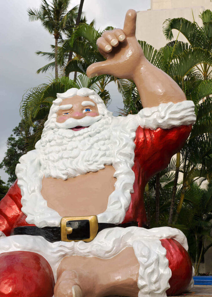 One of the best places to see Christmas lights in Hawaii is at Honolulu City Lights on Oahu. Image of a Santa statue throwing a shaka in Hawaii.