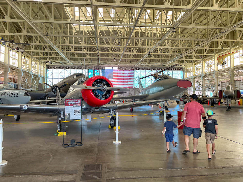 Interior of Hangar 79 of the Pearl Harbor Aviation Museum. Image of a dad and two little boys walking around the airplane museum.