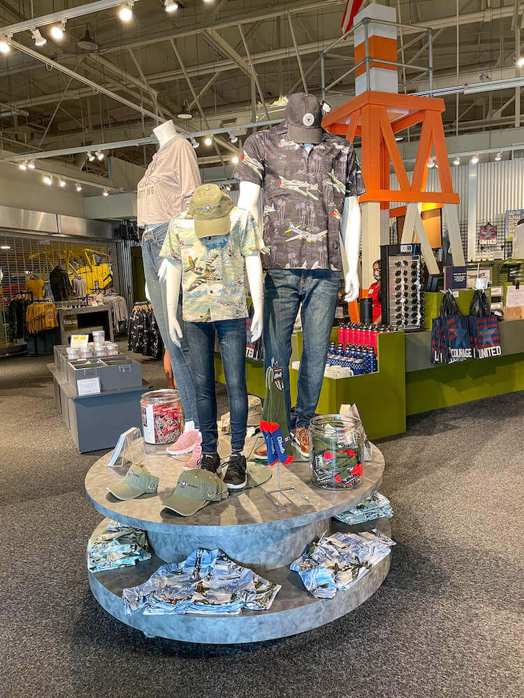 The Pearl Harbor Aviation Museum gift shop is full of all kinds of Pearl Harbor souvenirs. Image of a display of Aloha shirts, hats, and other airplane-themed items.