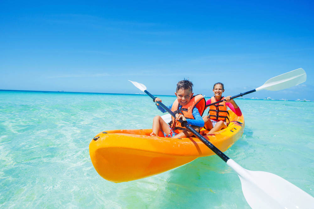 Get my top safety tips for kayaking in Hawaii as a family. Image of a mom and son wearing orange life vests and paddling a yellow kayak.