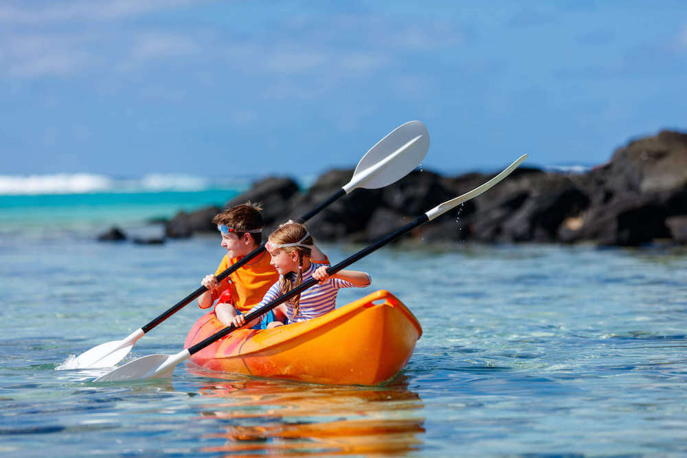 Get my top tips for kayaking in Hawaii with kids including how to choose the right boat and paddles for your family. Image of two kids in an orange kayak.