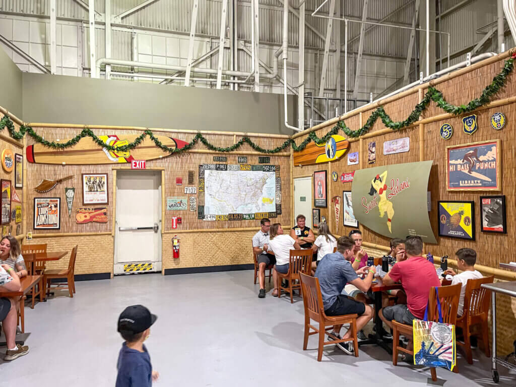 Image of a restaurant with WWII-era artwork hanging from walls covered with lauhala mats and dried grass.