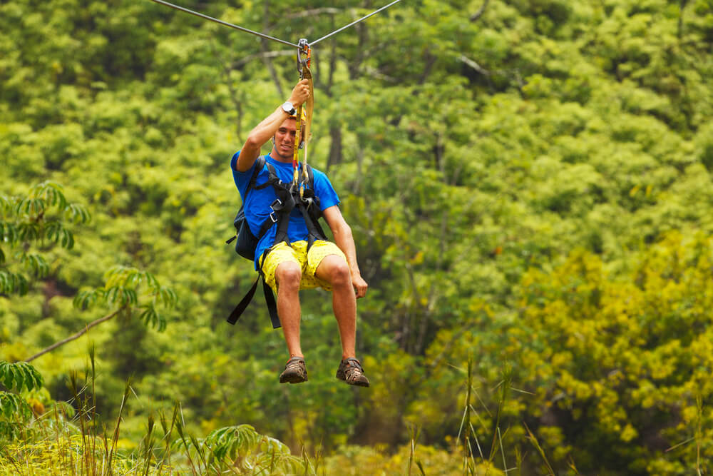 Find out where to go ziplining on Oahu Hawaii by top Hawaii blog Hawaii Travel with Kids. Image of a man wearing a blue shirt ziplining.