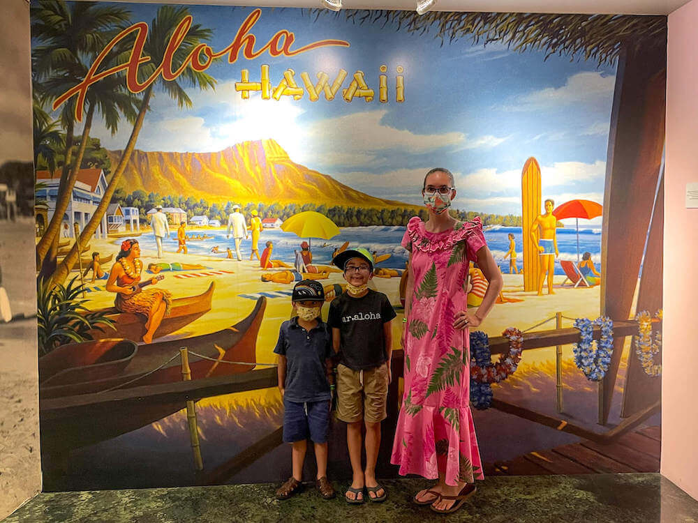 Wondering what to wear to Pearl Harbor? You can keep it casual with a t-shirt and shorts, or dress up a bit with Aloha wear. Image of a mom wearing a pink mu'u mu'u and two boys wearing t-shirts and shorts at the Pearl Harbor Aviation Museum.