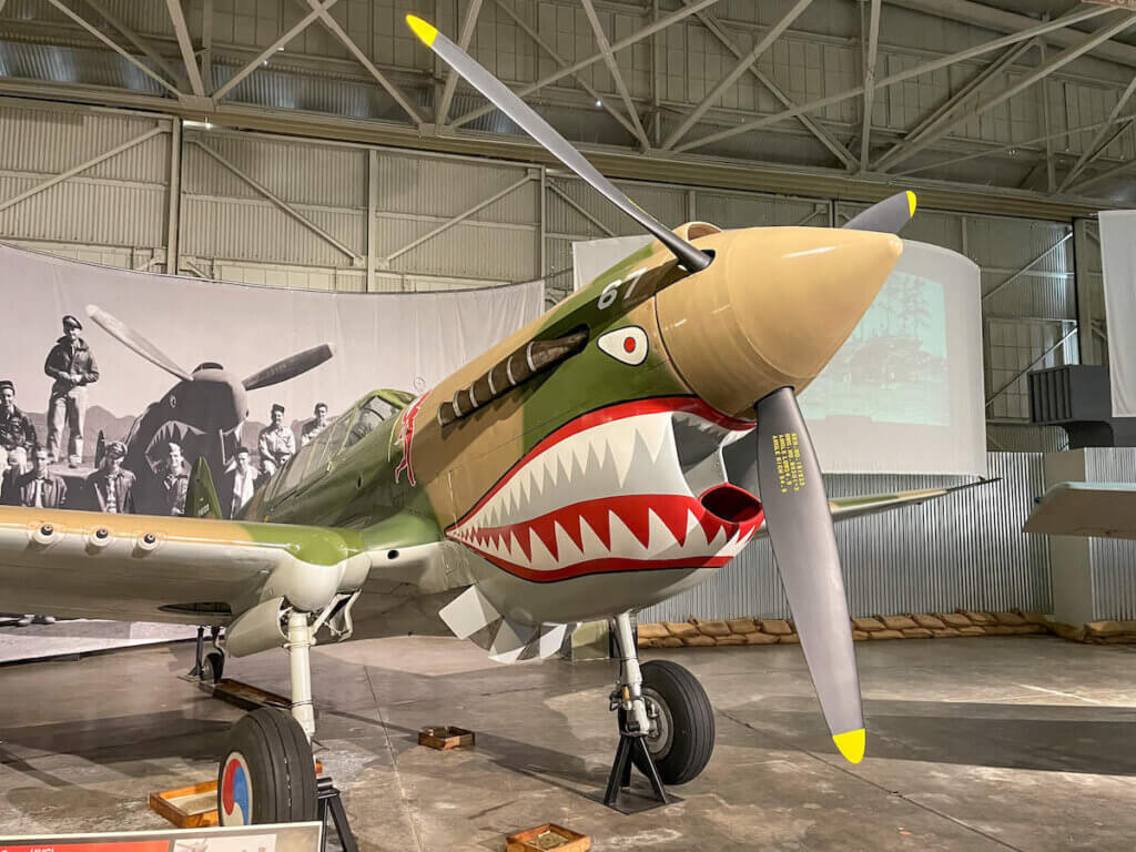 Planning to visit Pearl Harbor with kids? Read this Pearl Harbor Aviation Museum review by top Hawaii blog Hawaii Travel with Kids. Image of a WWII airplane painted with a face with sharp teeth.