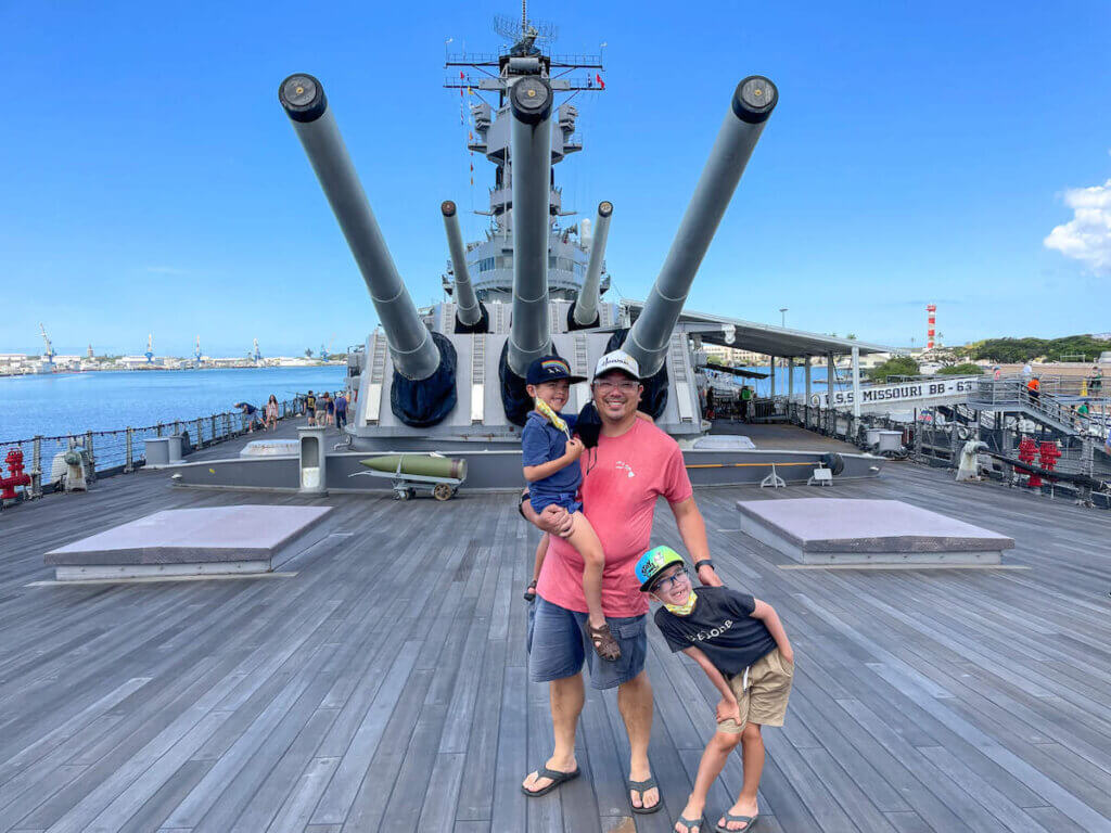 Find out whether or not it's worth visiting Pearl Harbor with kids by top Hawaii blog Hawaii Travel with Kids. Image of a dad and two boys posing on the deck of the USS Battleship Missouri