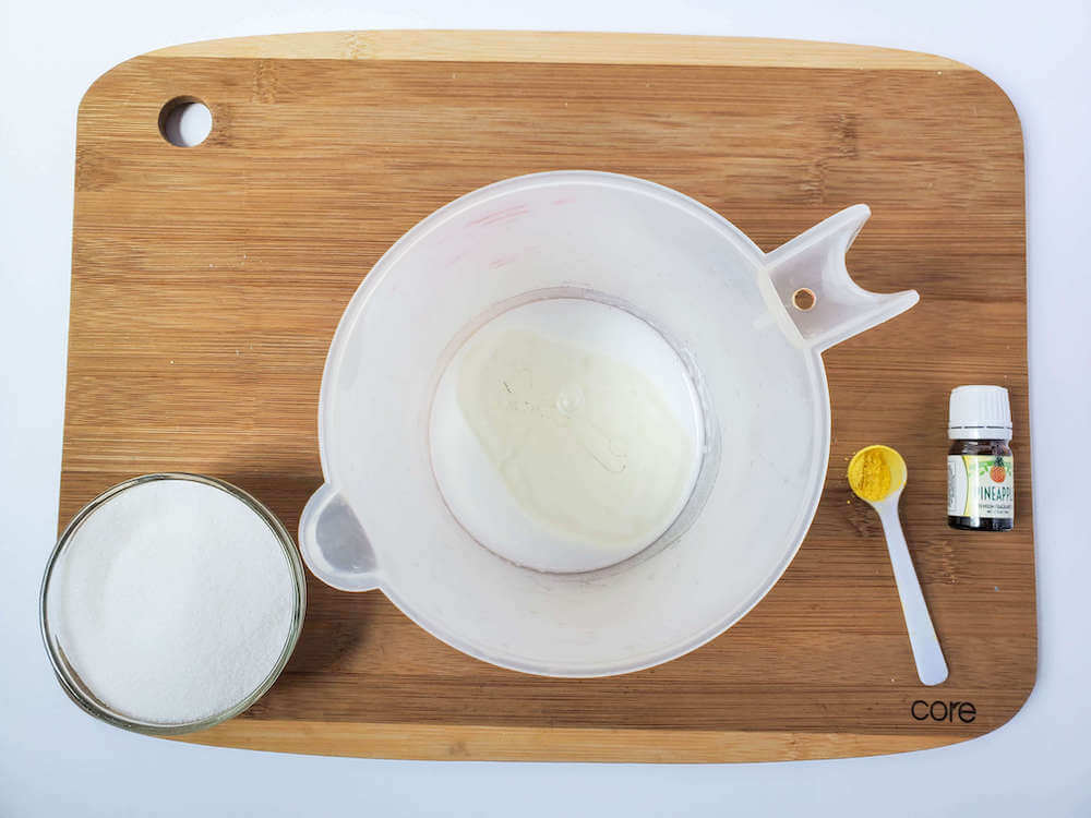 These are all the ingredients you'll need to make Hawaiian pineapple sugar scrub bars. Image of a white liquid measuring cup, sugar, mica powder, soap, and pineapple oil.