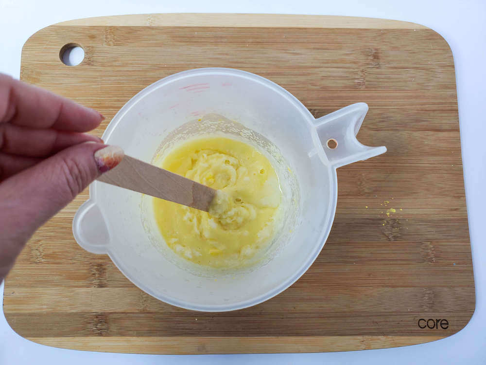 Make sure to thoroughly stir up your pineapple sugar scrub bar mixture. Image of someone stirring ingredients in a white liquid measuring cup.